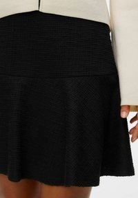 Jupe noire avec un motif texturé, présentant un design évasé et une taille ajustée. Assortie à un haut couleur crème.