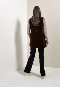 Kashmir vest vihreäva beige pitkiä hihoja ylle, yhdistetty mustiin housuihin ja vaaleisiin lenkkikenkiin. Yksinkertainen muotoilu, ei näkyviä kuvioita.