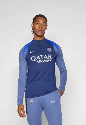 Haut de sport à manches longues marine avec des accents bleus, col zippé quart, et logo blanc "Qatar Airways"; associé à un pantalon de sport bleu.