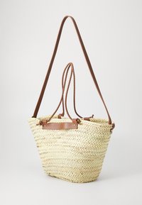 Ψαθένιο καλάθι με κωνικό σχήμα, σε ανοιχτό μπεζ χρώμα, με καφέ δερμάτινους ιμάντες ώμου και επίπεδη δερμάτινη διακόσμηση.