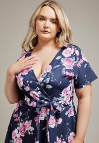Vestido envolvente floral en azul marino con rosas rosas. Presenta un escote en V profundo, mangas cortas y un lazo lateral. Tejido suave con un ligero brillo.