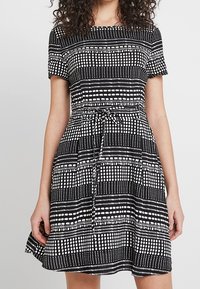 Svart och vit mönstrad klänning med korta ärmar, en figursydd bodice och en utsvängd kjol med dragsko i midjan.