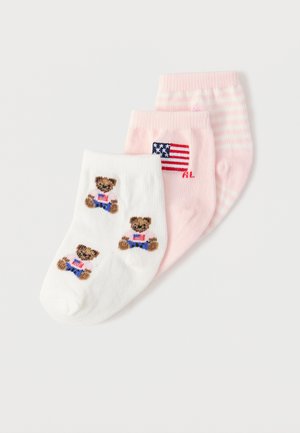 Tre par babysokker i hvitt med bamser, rosa med et amerikansk flagg, og rosa med hvite striper, arrangert overlappende.