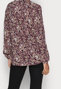 Blusa a maniche lunghe con motivo paisley in tonalità di bordeaux, crema e nero. Realizzata in tessuto morbido, presenta una vestibilità ampia e polsini arricciati.