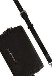 Sort læder crossover-taske med en struktureret form. Har et sølvfarvet "RETERNITY" logo og justerbar rem med hardware-detaljer.