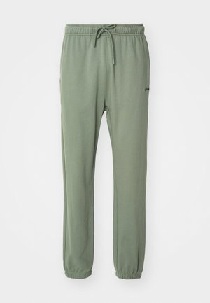 Green sweatpants featuring a drawstring waistband, elastic cuffs, and a smooth texture. The brand logo is displayed on the side.