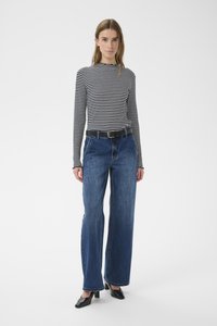 Gestreiftes Langarmshirt in Schwarz und Weiß, kombiniert mit weiten blauen Jeans, schwarzem Gürtel und schwarzen Mules mit Absatz.