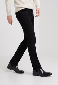 Black slim-fit jeans with a smooth texture, featuring a classic design and subtle stitching. Paired with shiny black dress shoes.