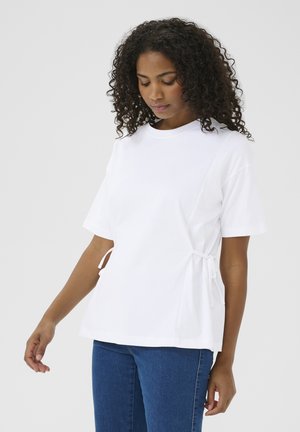 Hvid T-shirt lavet af bomuld. Har korte ærmer, rund hals og sidesnor for justering. Bruges med blå denimjeans.