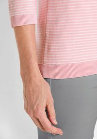 Hellrosa gestreifter Pullover mit gerippten Bündchen und Saum, kombiniert mit grauen Hosen. Fokus auf den horizontalen Streifen und die Texturdetails des Stoffes.