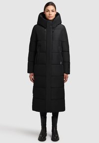 Czarna kurtka puchowa o długim, dopasowanym kroju, z dużym kapturem i kieszeniami zapinanymi na zamek. Gładka tekstura o matowym wykończeniu i pikowany wzór.