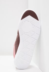 Idrottssko med en texturerad brun och rosa ovandel samt en vit gummisula med ett geometriskt mönster för bra grepp.