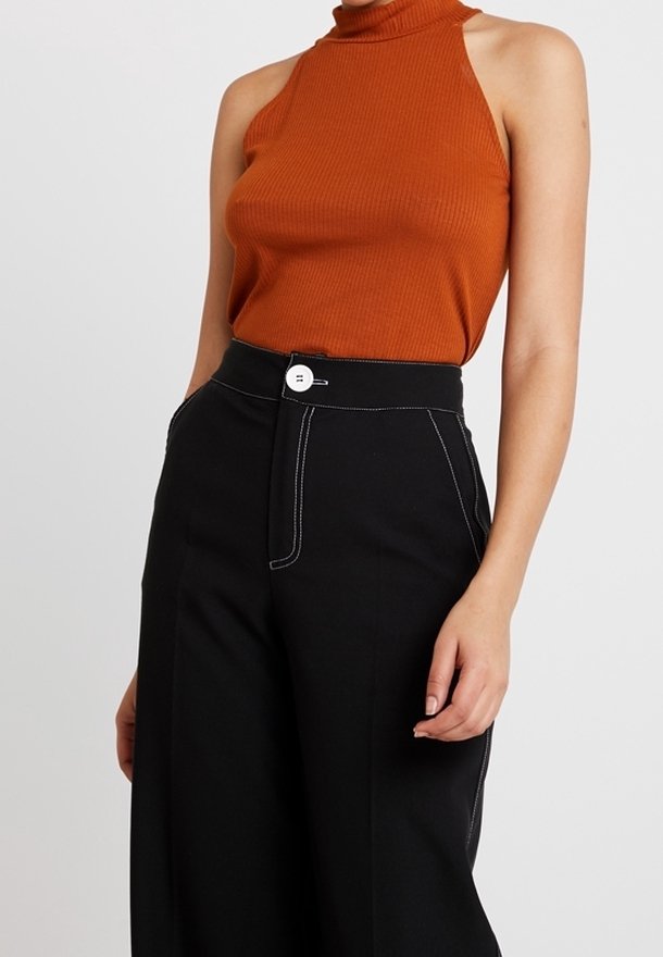 Top sin mangas de color naranja acanalado con cuello alto, combinado con pantalones negros de tiro alto que tienen costuras blancas y un botón blanco circular.