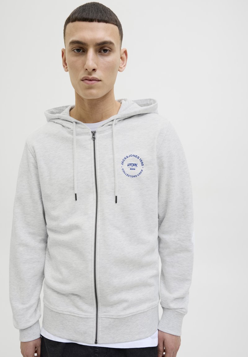 Sudadera gris con cremallera hecha de tela suave. Cuenta con una capucha con cordón, bolsillo frontal y un estampado gráfico azul. Cremallera negra y puños acanalados.