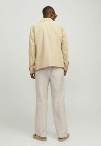 Chaqueta de lino beige con un corte relajado, y pantalones cremosos claros y texturizados con un patrón sutil, acompañados de calzado plano en un tono neutro.