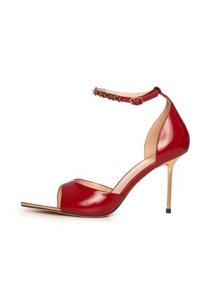 Sandalia de tacón alto de charol rojo con abertura en los dedos, tacón de aguja delgado dorado y correa en el tobillo con hebilla dorada y detalles de tachuelas.