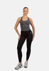 Sportoutfit bestaande uit een grijze getailleerde tanktop en hoge zwarte legging, aangevuld met grijs-witte sneakers.