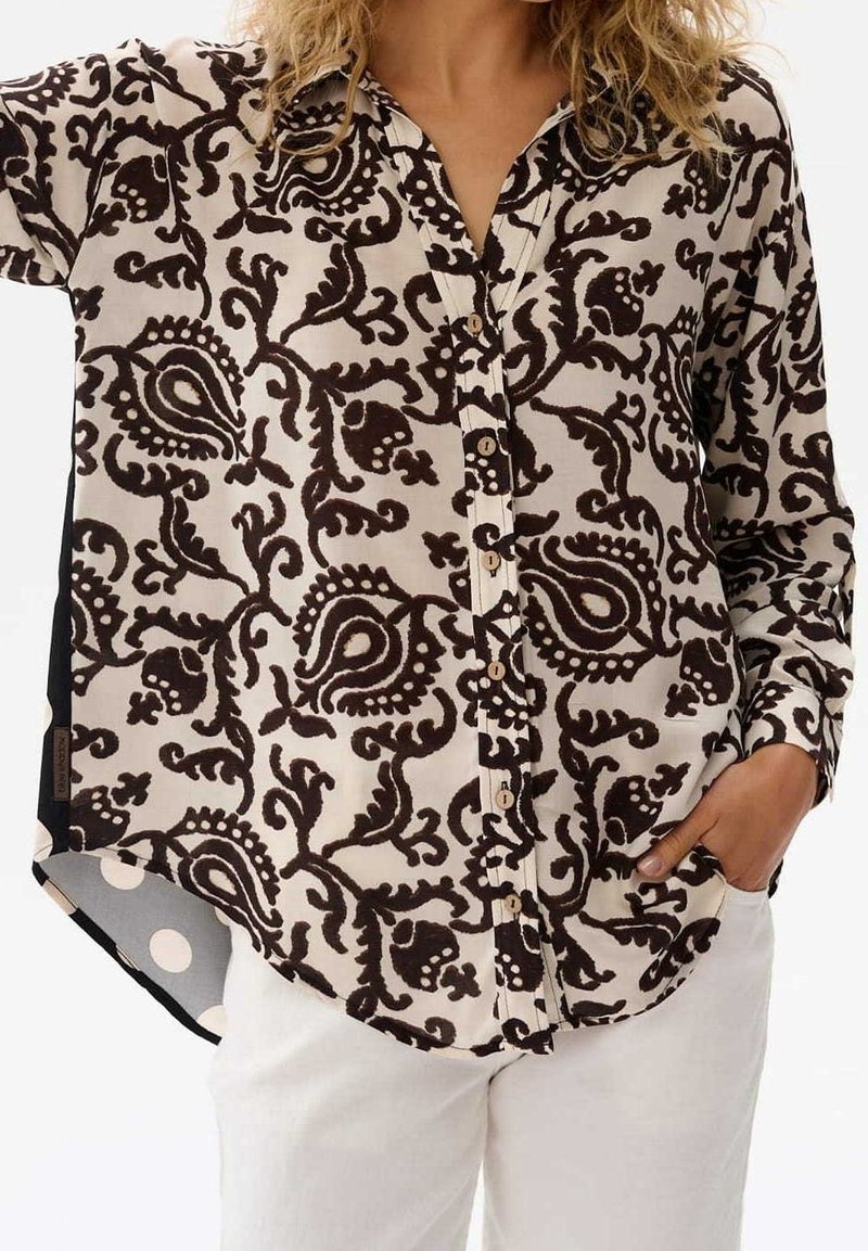 Camicia bottonata con un motivo paisley marrone su uno sfondo crema, con una vestibilità rilassata e aperture laterali. Decorata con bottoni in legno.