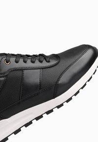 Sneaker nera con una combinazione di pelle liscia e parte superiore in mesh testurizzato, punta rotonda e suola in gomma bianca con battistrada decorato. Chiusura con lacci neri.