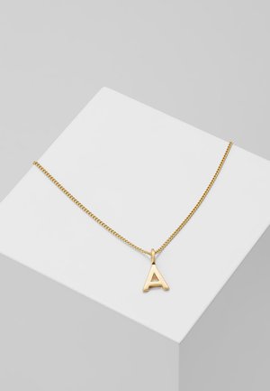 Collana d'oro con pendant a forma di lettera "A", caratterizzata da una finitura liscia e lucida e una catena sottile e testurizzata, esposta su un supporto geometrico bianco.