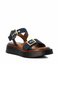 Platform sandal with black sole, brown footbed, navy blue denim straps, and gold-tone buckles on a white background.