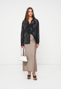 Blusa nera trasparente con motivi floreali blu e argento, abbinata a una gonna lunga beige. Borsa bianca e sandali neri con piattaforma.