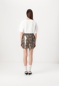 Witte T-shirt met korte mouwen, gecombineerd met een glanzende mini-rok met luipaardprint. De outfit heeft een gestructureerde stof en een aansluitende pasvorm.