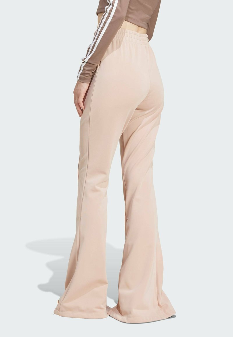 Pantalon évasé rose clair avec une taille élastique, texture lisse et détails de couture subtils. Le matériau semble léger et extensible.