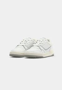 Bijele sportske cipele s perforiranim detaljima, sivoj obrubi i strukturiranim potplatima. Okroglasti dizajn s klasičnim vezanjem.