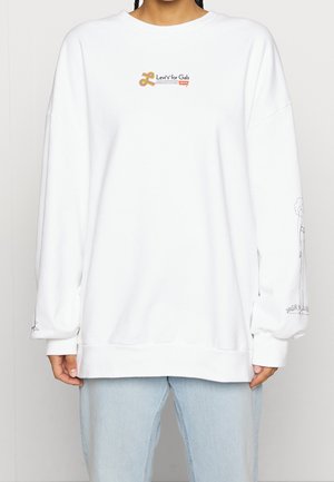 Sweat-shirt blanc oversize avec le logo « Levi's for Gals » sur la poitrine et des dessins en lignes noires sur la manche gauche, porté avec un jean bleu clair.