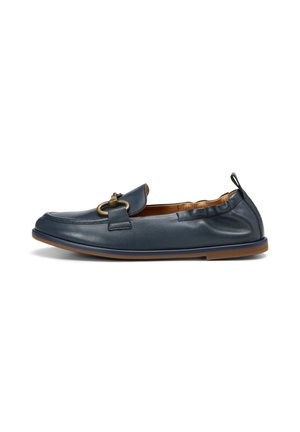 Mocassin en cuir bleu marine avec un dos élastique, une semelle marron et une boucle décorative en métal doré sur le dessus.