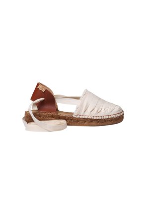 Witte canvas espadrille met een hiel van bruin leer, een gevlochten jutezool en een crème enkelsluiting op een witte achtergrond.