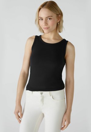 Zwarte geribbelde tanktop met een ronde halslijn en brede banden, aangevuld met witte slim-fit jeans met een sluiting met een knop aan de voorkant.