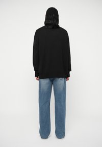 Črna pletena pulover s spuščenimi rameni, v kombinaciji s svetlo modrimi širokimi hlačami, ki imajo fajnen izgled in vidne zadnje žepke.