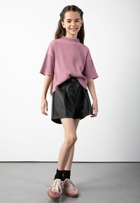 Różowa, prążkowana, oversize'owa koszulka z krótkim rękawem, czarna skórzana spódnica o wysokim talerzu oraz różowe trampki z białymi sznurowadłami i czarnymi skarpetami.