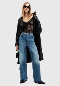 Body de encaje negro, vaqueros de mezclilla azules de gran tamaño y un largo abrigo de cuero negro. Los accesorios incluyen un pequeño bolso negro y gafas de sol.