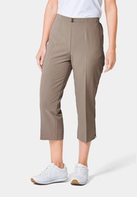 Khakifarbene Capri-Hosen mit glatter Textur, mittlerem Bund, Vorderfalten und Schlitzen am Saum. Kombiniert mit weißen Sport Schuhen.