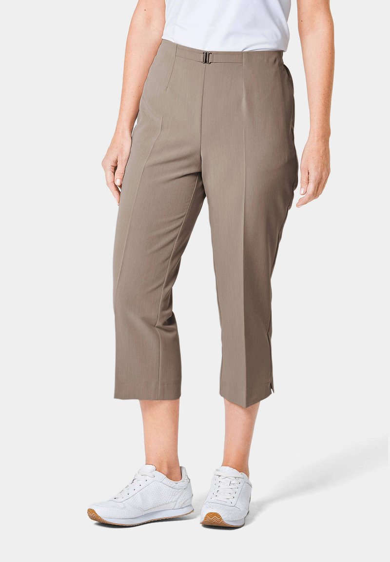 Khakifarbene Capri-Hosen mit glatter Textur, mittlerem Bund, Vorderfalten und Schlitzen am Saum. Kombiniert mit weißen Sport Schuhen.