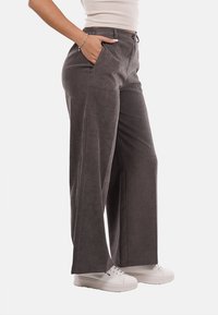 Pantaloni grigi a gamba larga con una finitura morbida e texturizzata; dotati di tasche laterali e vita elastica; abbinati a sneaker bianche.