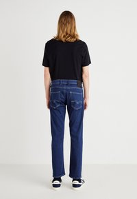 Jeans de mezclilla azul con un diseño de pierna recta, costuras en contraste y dos bolsillos traseros. Combinados con una camiseta negra básica y zapatillas.