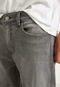 Grijze spijkerbroek van denim met een vervaagde afwerking, vijf zakken en een zilveren knoopsluiting bij de taille. Zachte textuur en subtiele stikdetails.