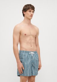 Swim shorts in light blue fabric with white vertical stripes and dots, featuring an elastic waistband and drawstring closure.