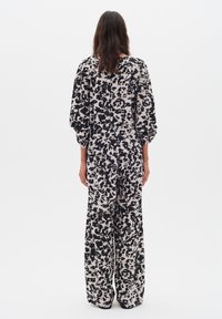 O femeie stând cu spatele la cameră, îmbrăcată cu un top loose alb-negru cu imprimeu abstract și pantaloni largi asortați.