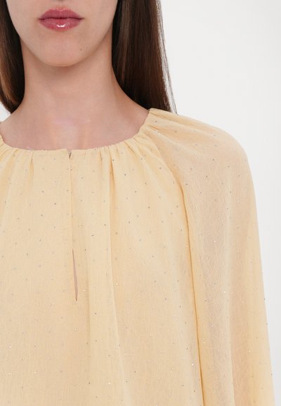 Geel blouse van een gestructureerde stof, met zilveren kleine stippen, geplooide halslijn en een sleutelgatuitsnede aan de voorkant.