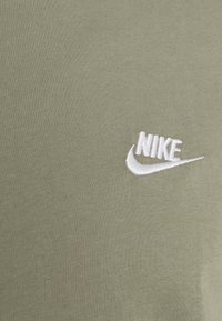 Olive zelené bavlněné tričko s bílým vyšívaným logem Nike. Hladká textura s jemným žebrováním, krátké rukávy a design s kulatým výstřihem.
