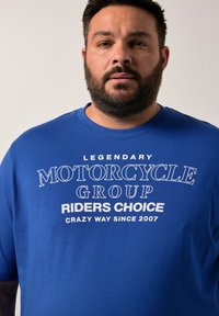 Modrá bavlněná tričko s bílým potiskem: "Legendární skupina motocyklových jezdců Volba bláznivého způsobu od roku 2007," s kulatým výstřihem a krátkými rukávy.
