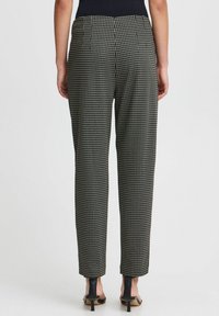 Pantalons à motif pied-de-poule noir et blanc avec une coupe décontractée, dotés d'une taille haute et de jambes fuselées, associés à des talons noirs.