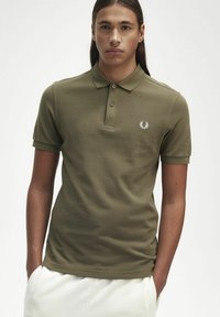 Polo shirt verde oliva in tessuto morbido, con colletto, maniche corte e logo ricamato bianco sul petto sinistro.
