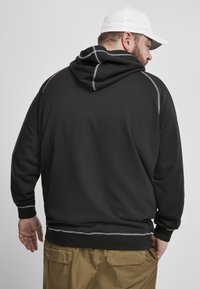 Felpa nera con cappuccio e coulisse, impreziosita da cuciture grigie a contrasto. Presenta una vestibilità comoda e polsini a costine, abbinata a pantaloni cargo beige.