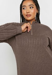 Brun ribbad zip-up tröja med långa ärmar, med hög krage och ett strukturerat mönster på tyget.